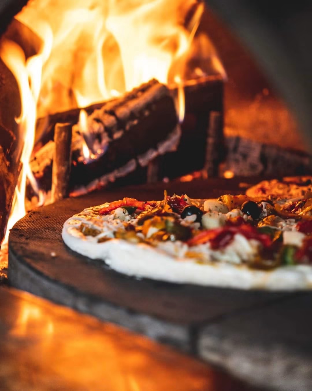 Pizza artisanale en cuisson devant les flammes du four à bois
